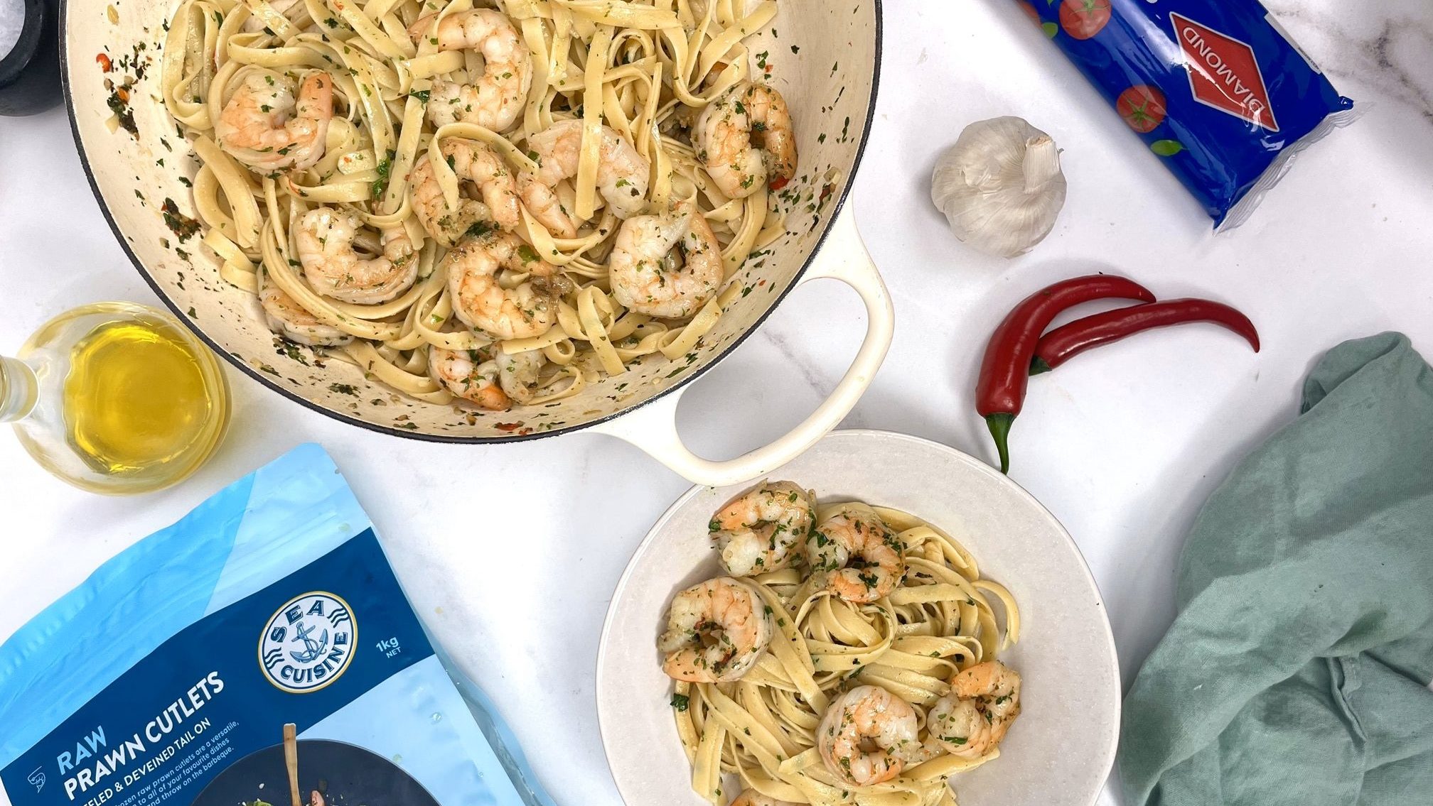 A pot and a plate of pasta with prawns and packs of prawns and pats by sides.