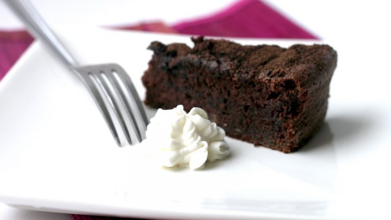 A piece of chocolate cake with cream on white plate with a fork.