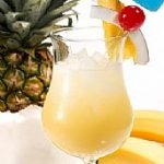 A tall stemmed glass of yellow drink with ice and a pineapple