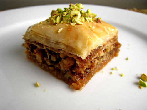 A piece of Baklava topped with pistachio on white plate.