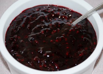 Dark red berry jam in a white dish with a spoon