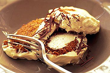 Three slices of biscuit cake covered with cream in a bowl with a fork