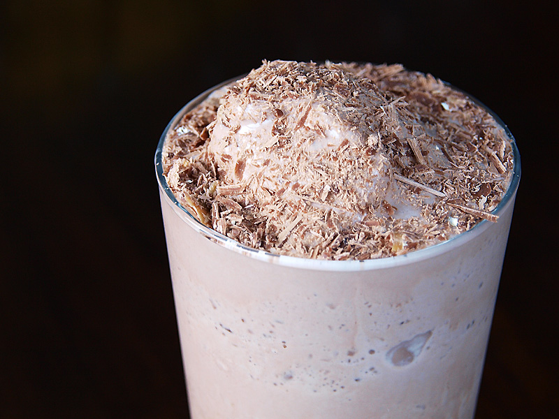 A cup of milky drink with some frothy top and chocolate shavings scattered.