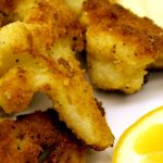 Crumbed Cauliflower pieces and lemon wedge on white plate.