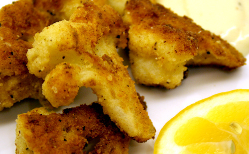 Crumbed Cauliflower pieces and lemon wedge on white plate.