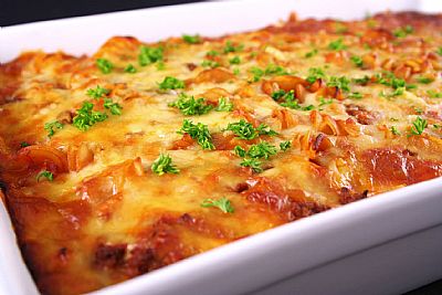 Cooked whole lasagne in white dish topped with green herbs.