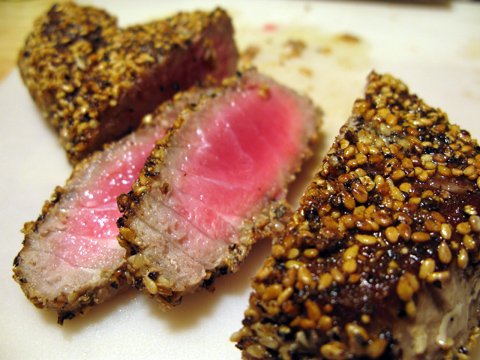 A piece of sesame seed coated tuna fish sliced, showing pink flesh inside.