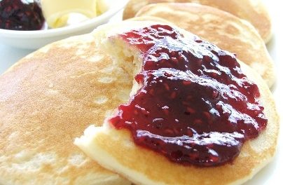 pikelets on a plate with strawberry jam on one and a side of butter