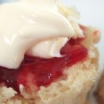 A slice of scone topped with red jam and cream