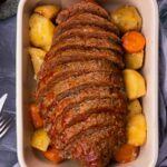 Sliced meatloaf in a dish with potatoes and carrots