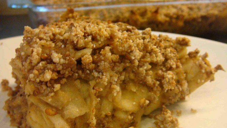 A portion of crumble on a plate in front and the glass baking dish full at rear.
