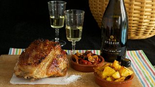A big roast meat, a bowl each of potato and vegetable, two glasses of white wine and a wine bottle