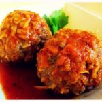 Two tomato sauce covered meat balls with some sauce and herb.