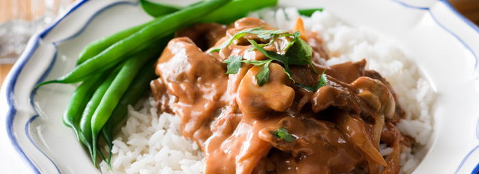Cooked meat and mushroom with sauce over white rice with green beams.