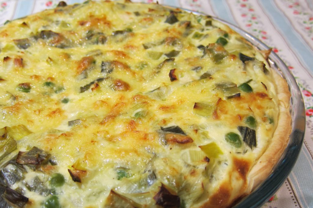 A round quiche with green vegetables bits showing.