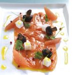 Cured salmon topped with cubes of white food and black olives , drizzle of oil.