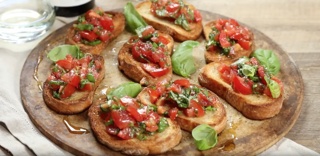 Eight pieces of bread topped with tomatoes and herb on wooden board.