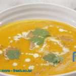 Pumpkin soup served in a white bowl with drizzled with cream and herbs.