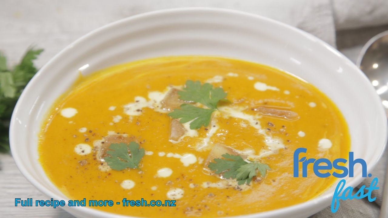 Pumpkin soup served in a white bowl with drizzled with cream and herbs.
