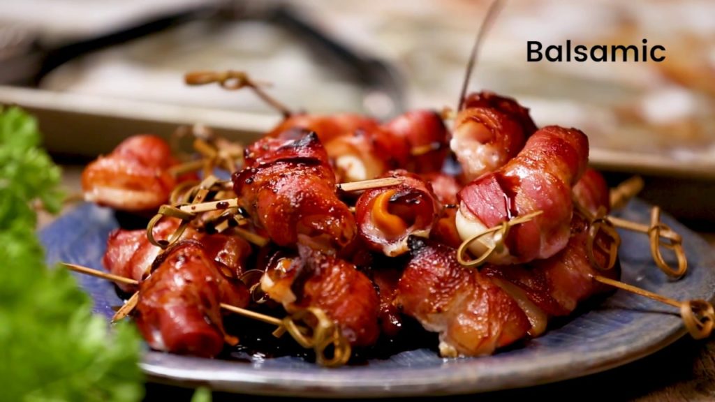 several bacon wrapped food skewers on a plate, greens in front.