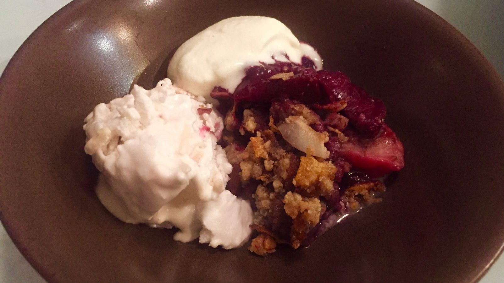 Plum crumble and white ice cream on brown bowl.