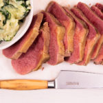 Sliced corned beef on a chopping board with spinach mash