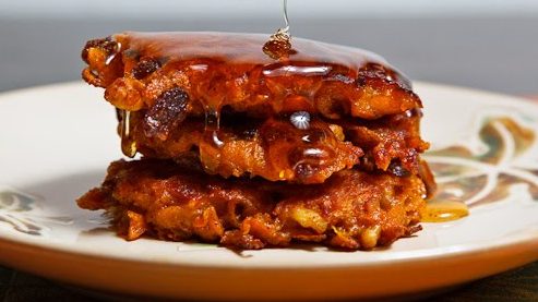 Three fritters stack on a plate, clear syrup pouring from top.