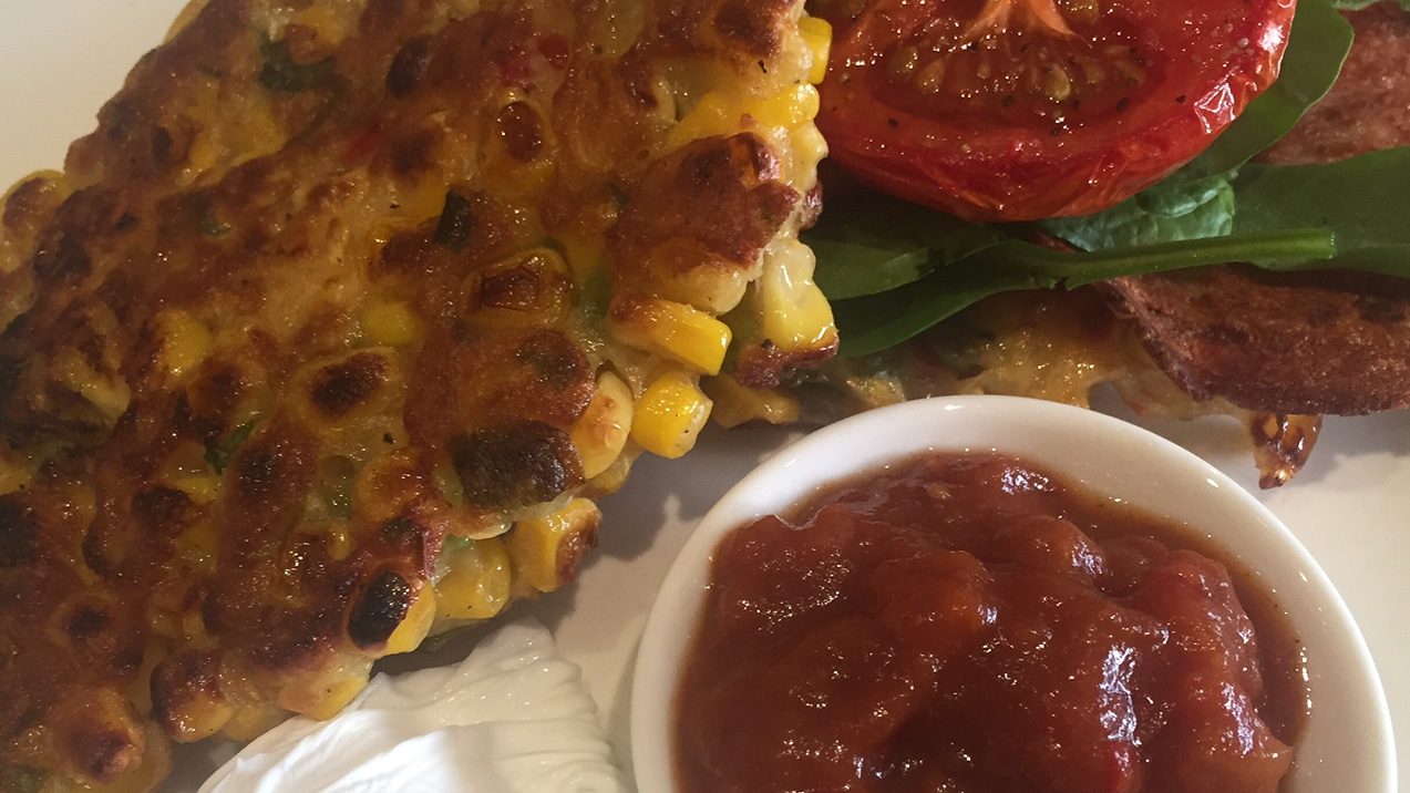 Corn fritters, tomato and a small bowl of red sauce on a plate.