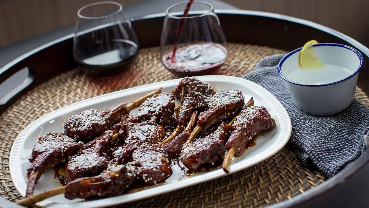Cooked lamb chops with dark brown sauce on white plate and two glasses of red wine.
