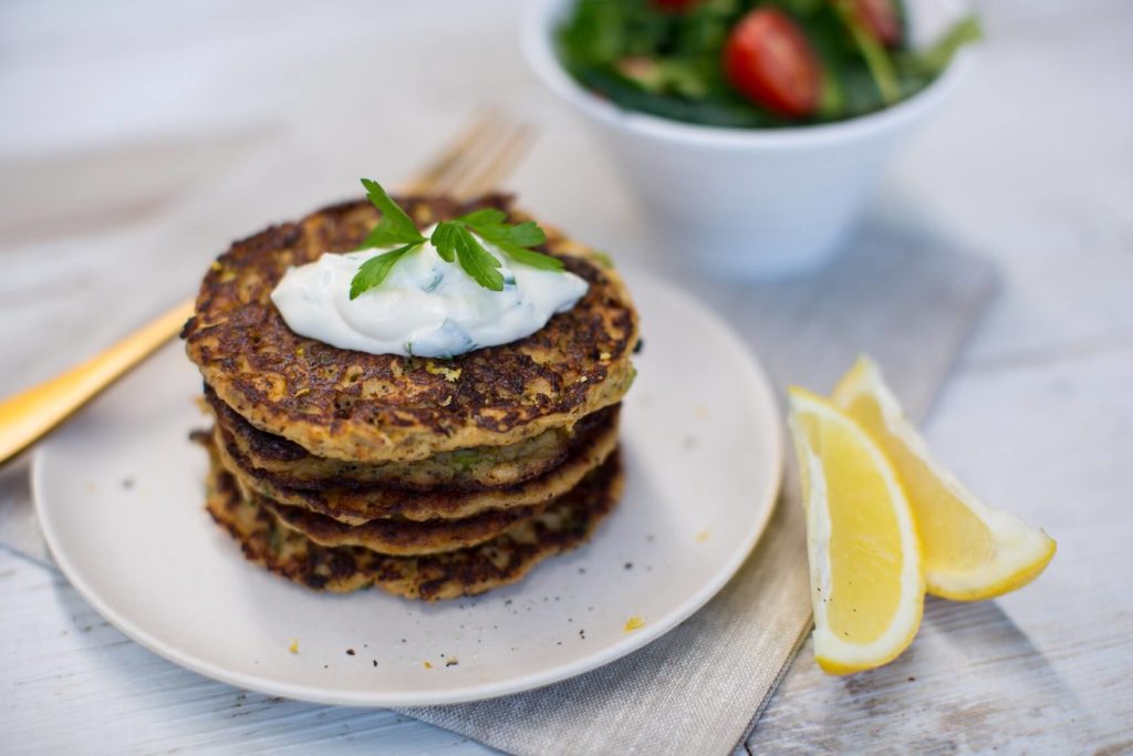 Stack of mussel fritters with a couple of lemon wedges, a fork and a small bowl of salad behind
