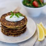 Stack of mussel fritters with a couple of lemon wedges, a fork and a small bowl of salad behind