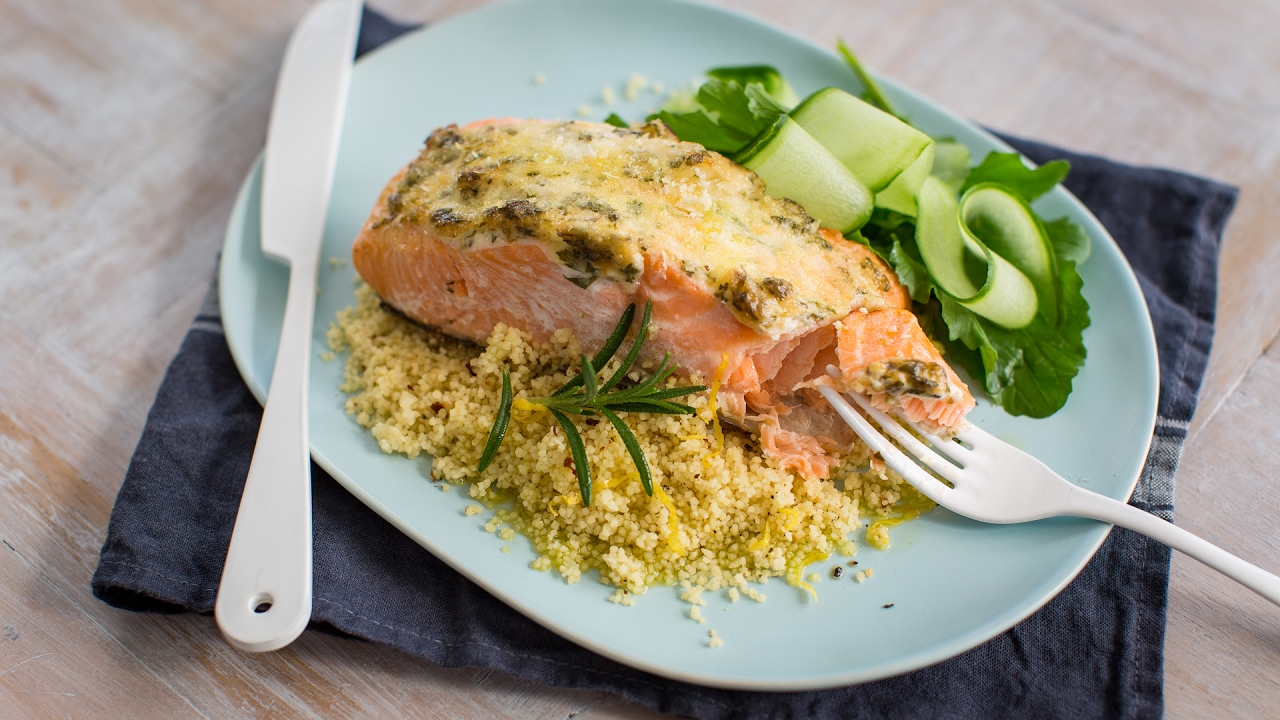 A piece of cooked salmon on yellow couscous and greens on a blue plate.