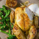 Roast whole chicken, bloccolini and lemon on a board