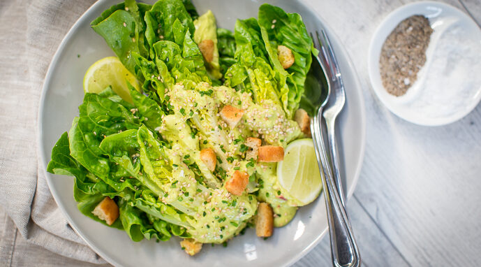 Cos lettuce topped with croutons and dressing with cut lemon, salt and pepper in small plate