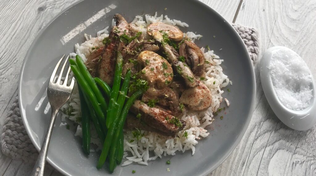 Beef and mushroom stroganoff on white rice with asparagus on grey round plate.