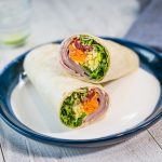 Two wraps filled with ham and salad stack on blue plate.
