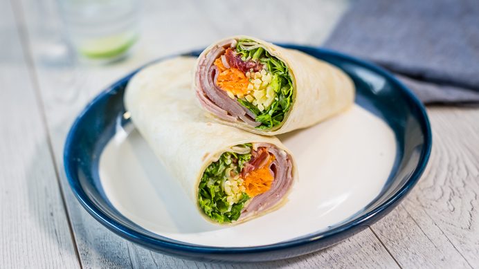 Two wraps filled with ham and salad stack on blue plate.