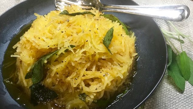 Yellow spaghetti like squash vegetable heap on black plate with herbs and spoon.