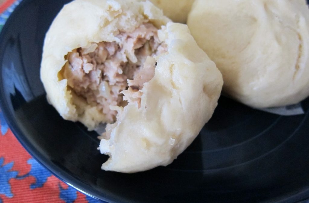 Pork buns on a plate with one torn in half.