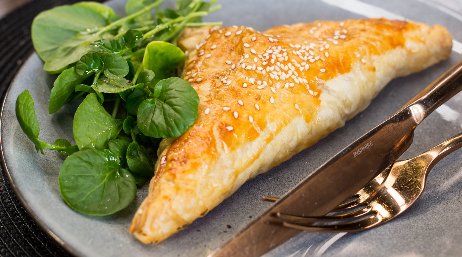 A triangle shaped baked pie on a plate with greens.