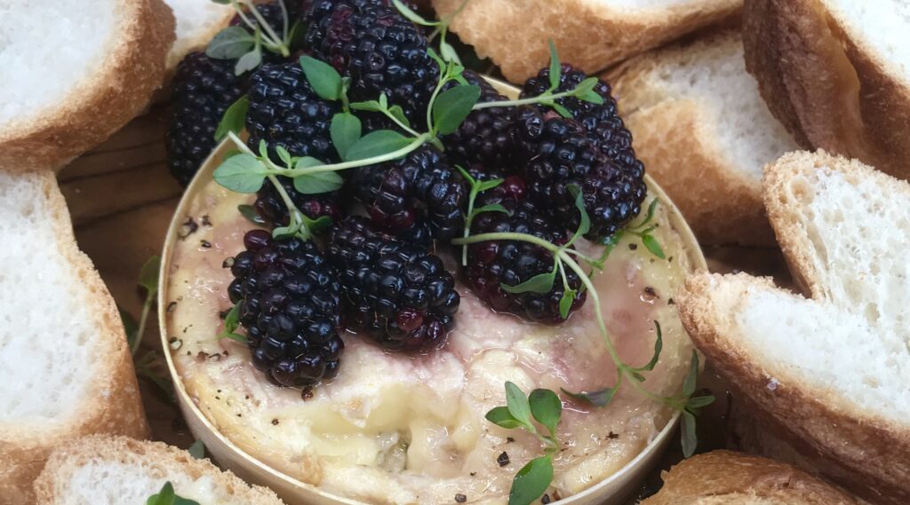 Creamy round cheese topped with berries and herb surrounded by sliced white bread