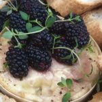 Creamy round cheese topped with berries and herb surrounded by sliced white bread