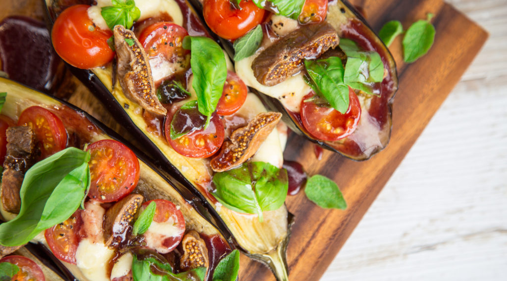 Grilled Eggplant with Tomatoes and Figs covered in basil on wooden board