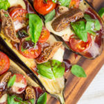 Grilled Eggplant with Tomatoes and Figs covered in basil on wooden board