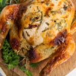 A whole roast chicken with herbs on wooden board.