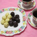 Dark chocolate and white chocolate truffles on a plate with two cups& saucers of tea.