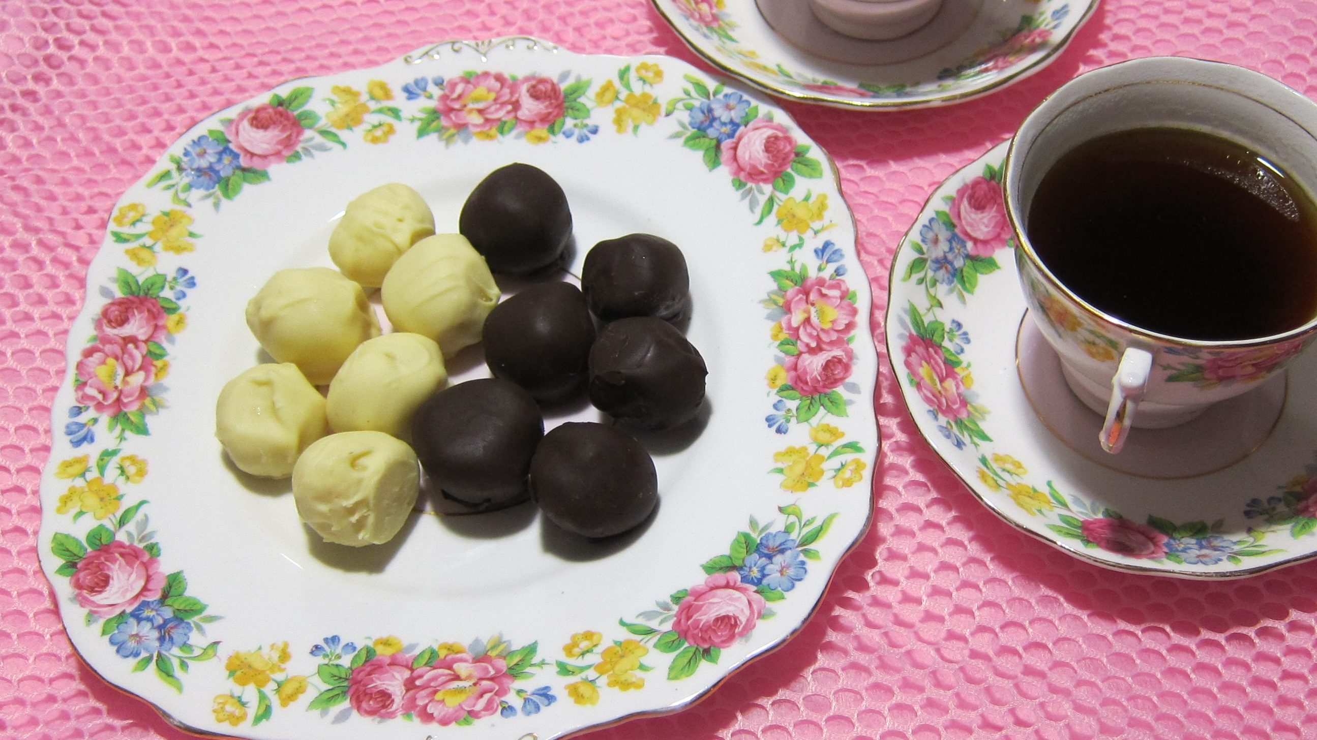 Dark chocolate and white chocolate truffles on a plate with two cups& saucers of tea.