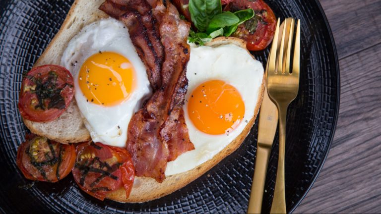 Two fried eggs, bacon and cooked tomatoes with herb on a plate with knife and fork.