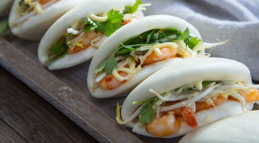 Four prawn and fresh green bao buns on wooden tray with dipping sauce