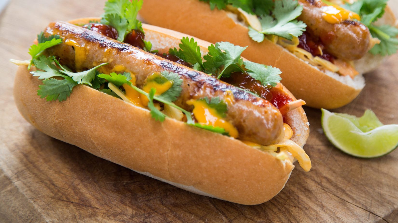 Hot dog with sriracha hot sauce garnished with coriander on a wooden board